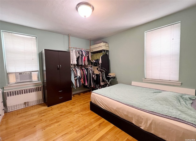 bedroom with radiator heating unit, light wood-type flooring, a closet, and cooling unit