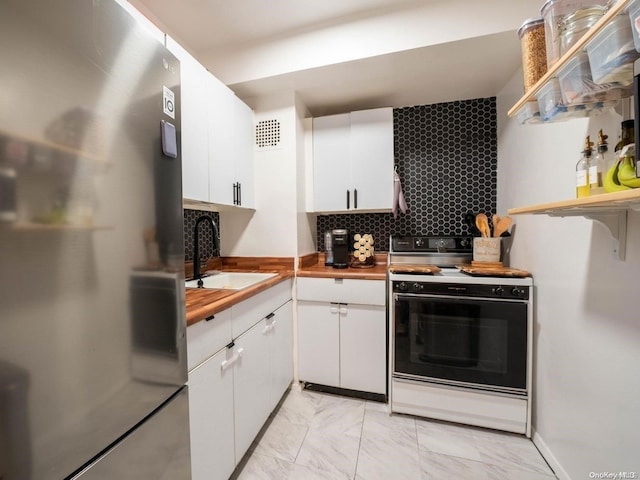 kitchen with decorative backsplash, white range, sink, white cabinetry, and stainless steel refrigerator