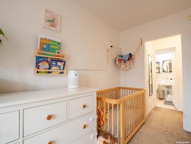 bedroom with ensuite bathroom, light colored carpet, and a nursery area