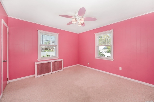 carpeted empty room with a wealth of natural light, radiator heating unit, ceiling fan, and ornamental molding