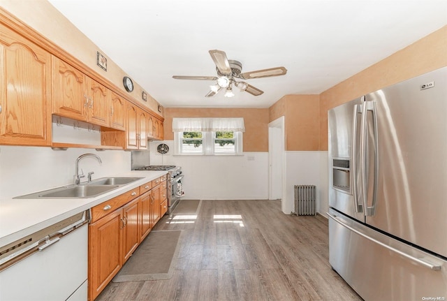 kitchen with radiator, ceiling fan, sink, light hardwood / wood-style floors, and appliances with stainless steel finishes