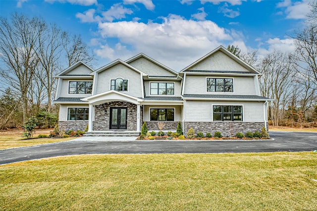 view of front facade with aphalt driveway, french doors, stone siding, and a front lawn