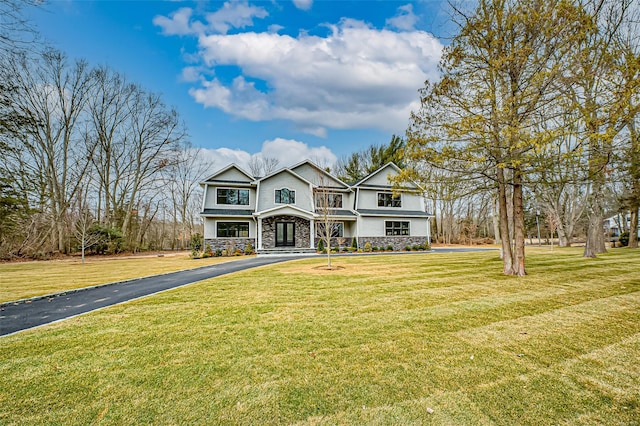 traditional-style home featuring aphalt driveway, stone siding, and a front lawn