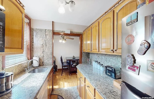 kitchen with light stone countertops, stainless steel fridge, light wood-type flooring, ceiling fan, and sink