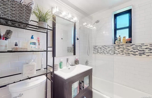 full bathroom with tasteful backsplash, toilet, shower / bath combination with glass door, vanity, and tile walls