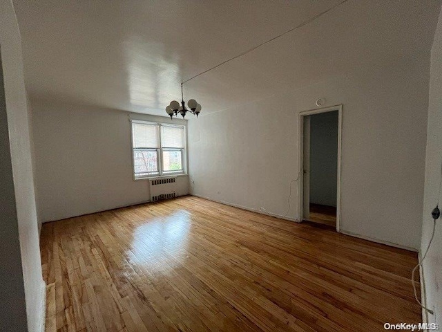 empty room featuring a notable chandelier, light hardwood / wood-style floors, and radiator