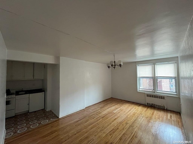 additional living space with light wood-type flooring, radiator, and an inviting chandelier