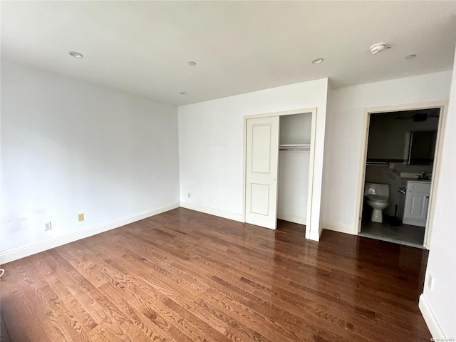 unfurnished bedroom featuring ensuite bathroom, a closet, and dark wood-type flooring