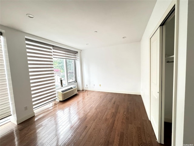 unfurnished bedroom with dark hardwood / wood-style floors, a wall mounted AC, and a closet