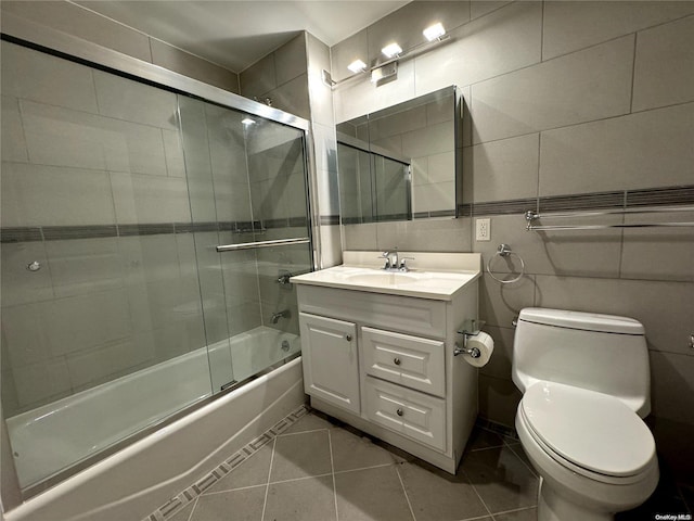 full bathroom featuring vanity, shower / bath combination with glass door, tile patterned floors, toilet, and tile walls