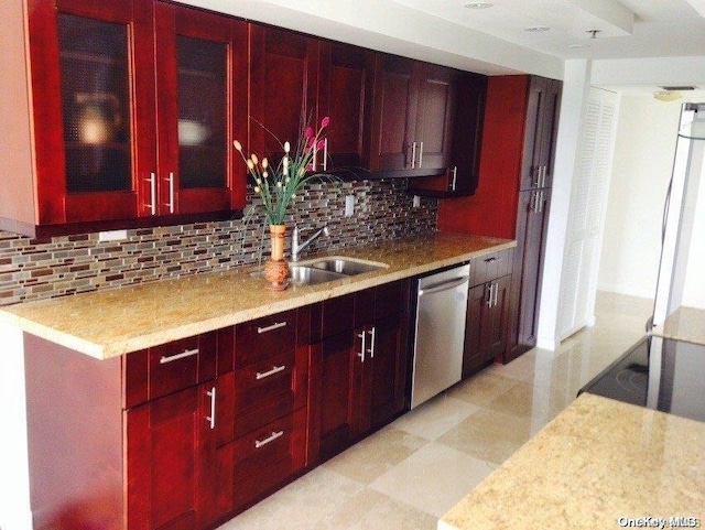 kitchen featuring light stone countertops, backsplash, stainless steel dishwasher, and sink