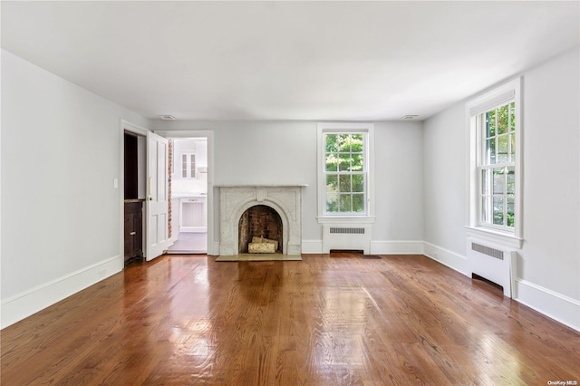 unfurnished living room with radiator, a premium fireplace, and hardwood / wood-style flooring