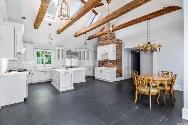 kitchen featuring white cabinetry, beamed ceiling, built in refrigerator, pendant lighting, and a kitchen island with sink