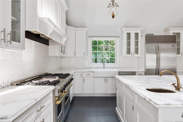 kitchen with backsplash, high end appliances, white cabinetry, and sink