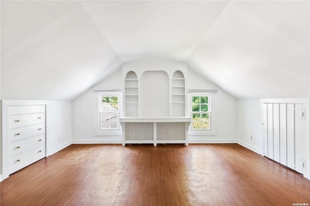 additional living space featuring built in features, hardwood / wood-style flooring, vaulted ceiling, and a healthy amount of sunlight