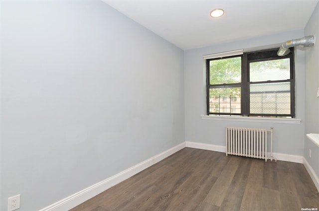 empty room with dark wood-style flooring, radiator, and baseboards