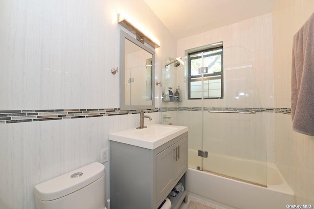 bathroom with tile walls, combined bath / shower with glass door, vanity, and toilet