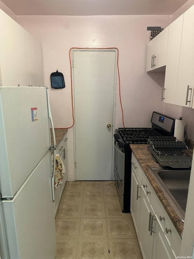 kitchen featuring white cabinetry, sink, white fridge, and stainless steel range with gas stovetop