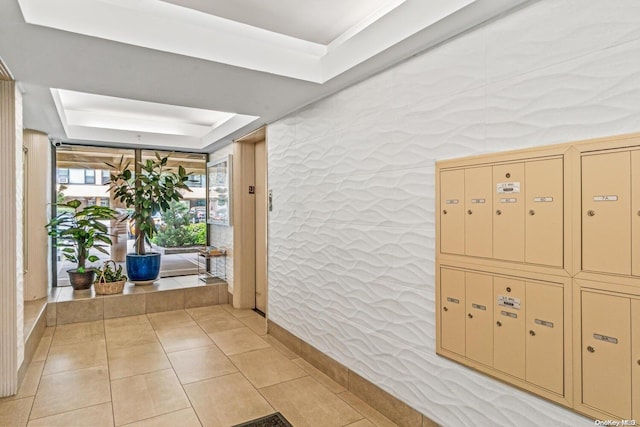 hallway featuring a tray ceiling, light tile patterned flooring, and a mail area