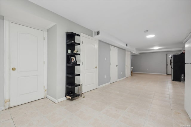 basement with light tile patterned floors and black fridge