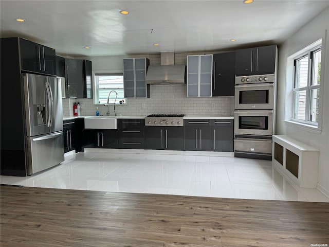 kitchen with decorative backsplash, appliances with stainless steel finishes, sink, wall chimney range hood, and light tile patterned floors