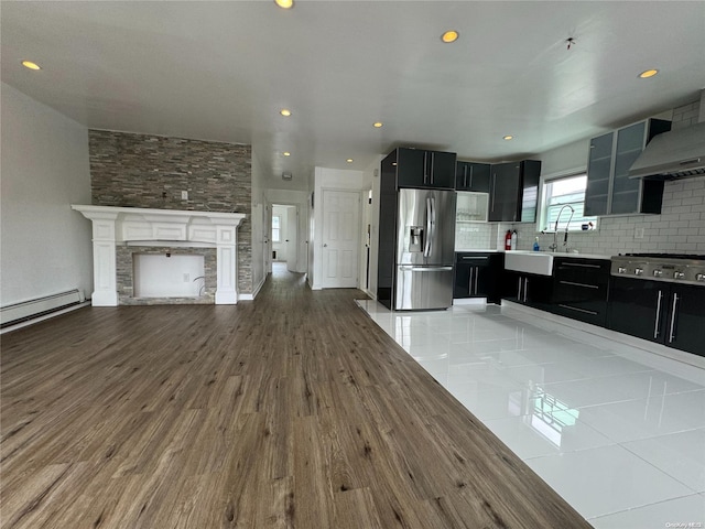 kitchen with decorative backsplash, appliances with stainless steel finishes, ventilation hood, baseboard heating, and a fireplace