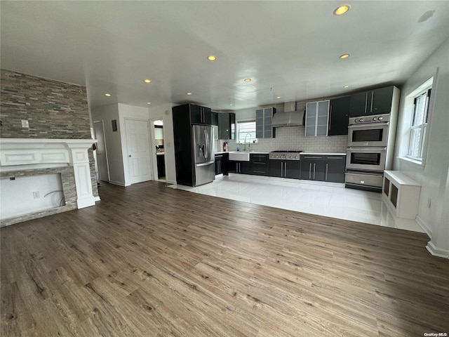 kitchen with a center island, wall chimney exhaust hood, stainless steel appliances, sink, and decorative backsplash