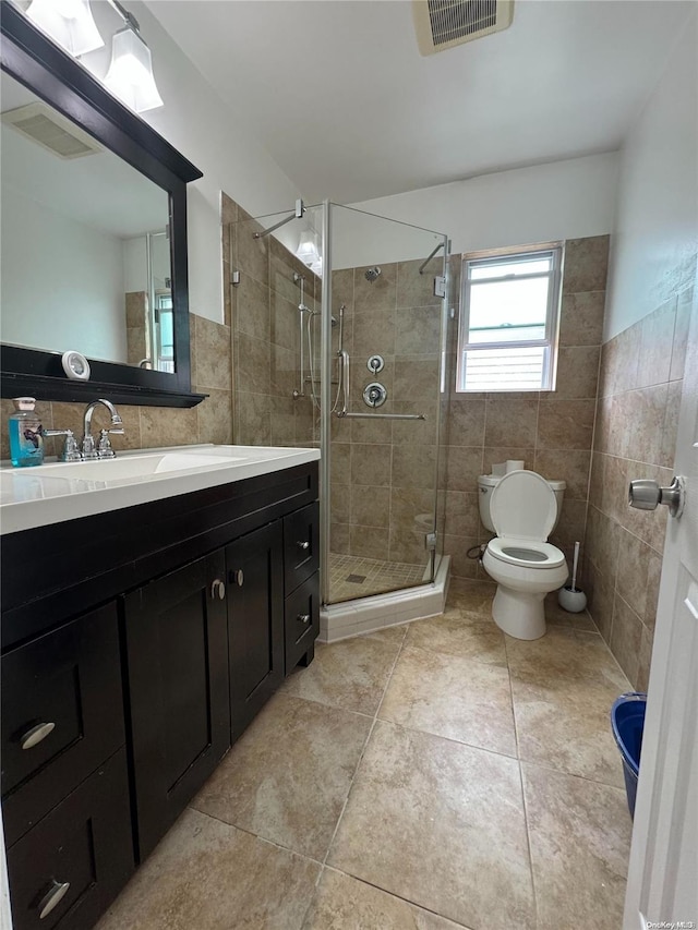 bathroom with tile patterned floors, toilet, a shower with door, vanity, and tile walls