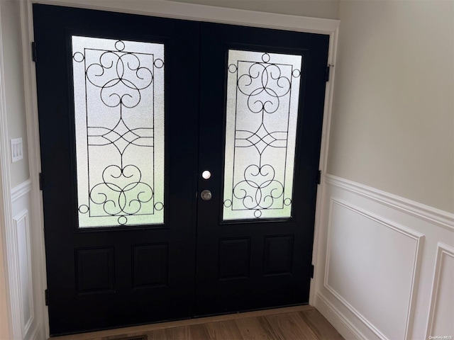 foyer entrance with a wainscoted wall, french doors, wood finished floors, and a decorative wall