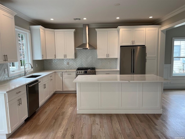 kitchen with sink, a kitchen island, stainless steel appliances, and wall chimney range hood