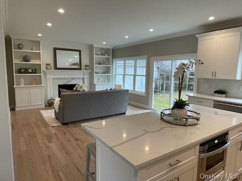 kitchen with oven, a premium fireplace, light hardwood / wood-style floors, light stone counters, and white cabinetry