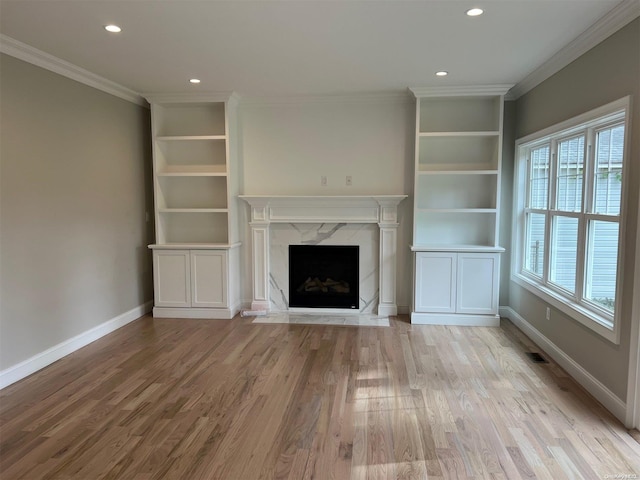 unfurnished living room featuring a high end fireplace, light wood-type flooring, and ornamental molding