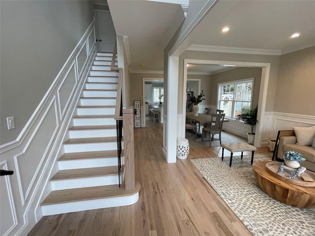 stairway with crown molding, recessed lighting, a decorative wall, wainscoting, and wood finished floors