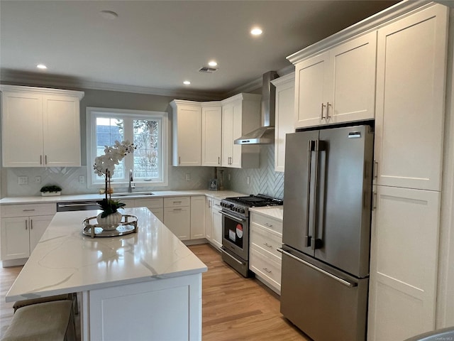 kitchen with stainless steel appliances, a center island, white cabinetry, and wall chimney range hood