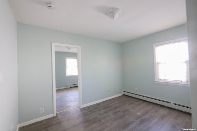 unfurnished room with a wealth of natural light, wood-type flooring, and a baseboard heating unit