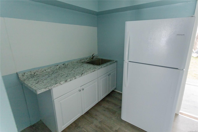 kitchen featuring light stone counters, sink, wood-type flooring, white fridge, and white cabinetry