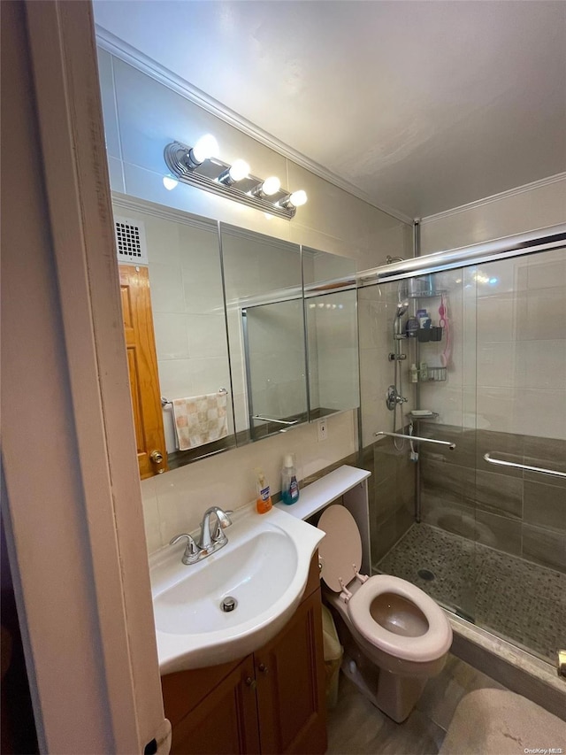 bathroom with vanity, toilet, a shower with shower door, and ornamental molding