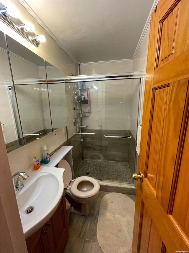 bathroom with vanity, toilet, a shower with shower door, and crown molding