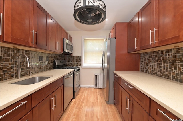 kitchen with sink, light stone counters, light hardwood / wood-style flooring, appliances with stainless steel finishes, and radiator heating unit