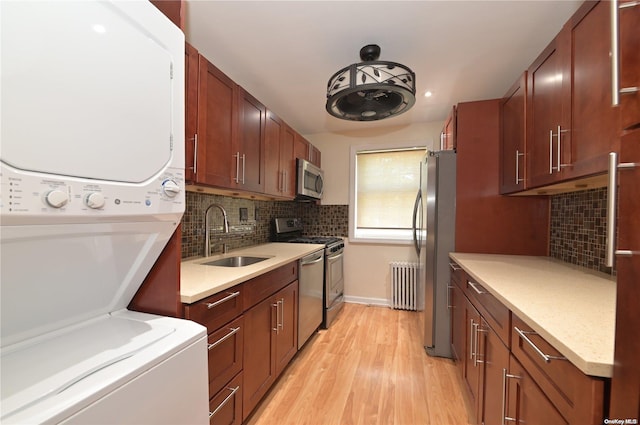 kitchen featuring appliances with stainless steel finishes, light countertops, light wood-type flooring, stacked washing maching and dryer, and a sink