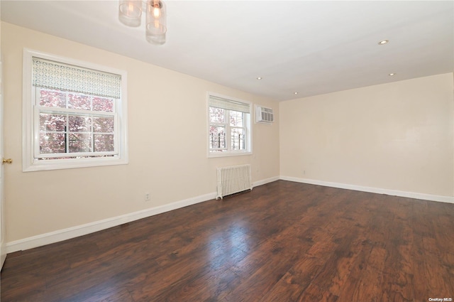 empty room featuring radiator, dark wood-type flooring, and a wall unit AC