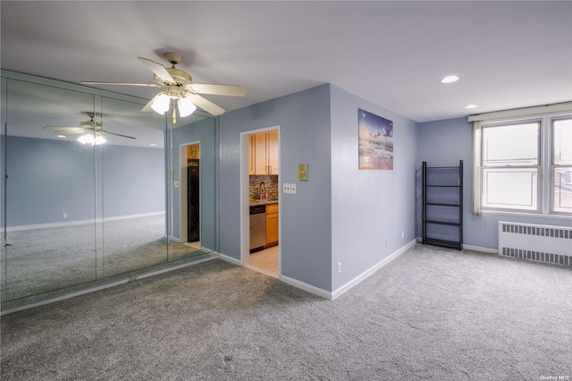 spare room with light colored carpet, radiator, and ceiling fan