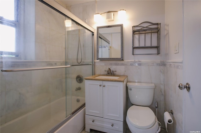 full bathroom featuring vanity, bath / shower combo with glass door, tile walls, and toilet