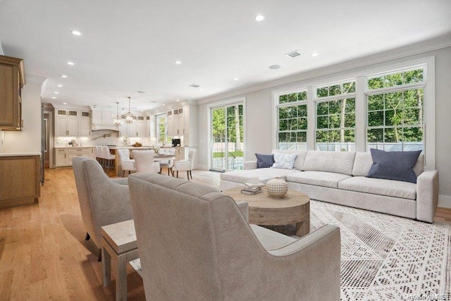 living room featuring light wood-type flooring, an inviting chandelier, plenty of natural light, and crown molding