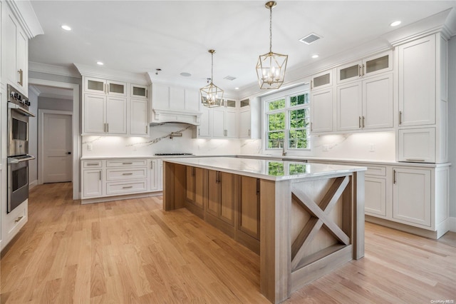 kitchen featuring white cabinets, light wood-type flooring, a center island, and double oven