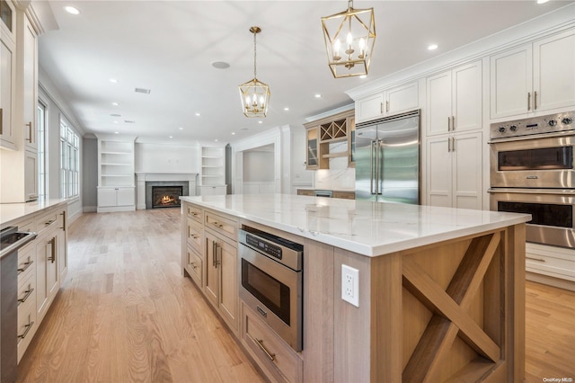 kitchen featuring appliances with stainless steel finishes, light wood-type flooring, pendant lighting, white cabinets, and a large island