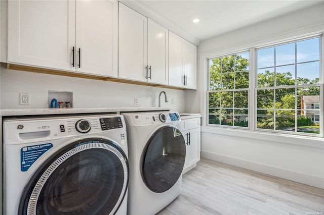 clothes washing area with cabinets, light hardwood / wood-style floors, and washing machine and dryer