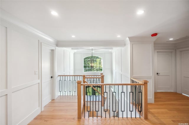 hall with light hardwood / wood-style flooring, a notable chandelier, and ornamental molding