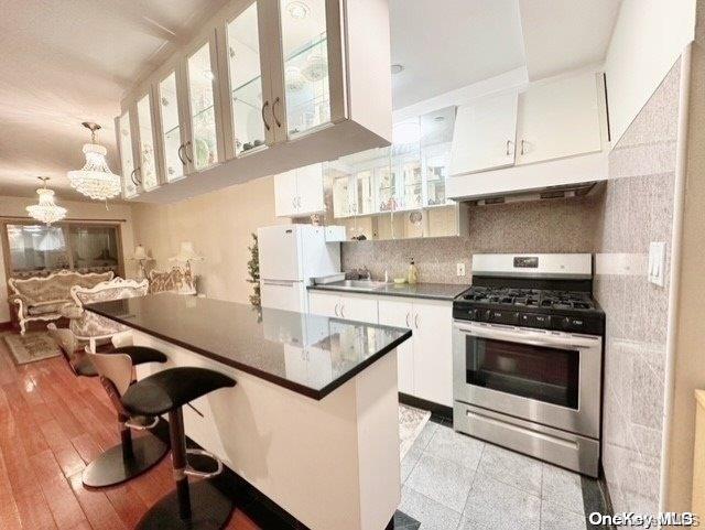 kitchen with white cabinetry, stainless steel gas range oven, white refrigerator, decorative backsplash, and light wood-type flooring