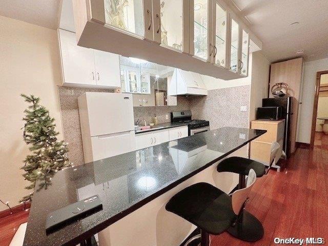 kitchen featuring a breakfast bar, white refrigerator, stainless steel stove, dark stone countertops, and white cabinetry